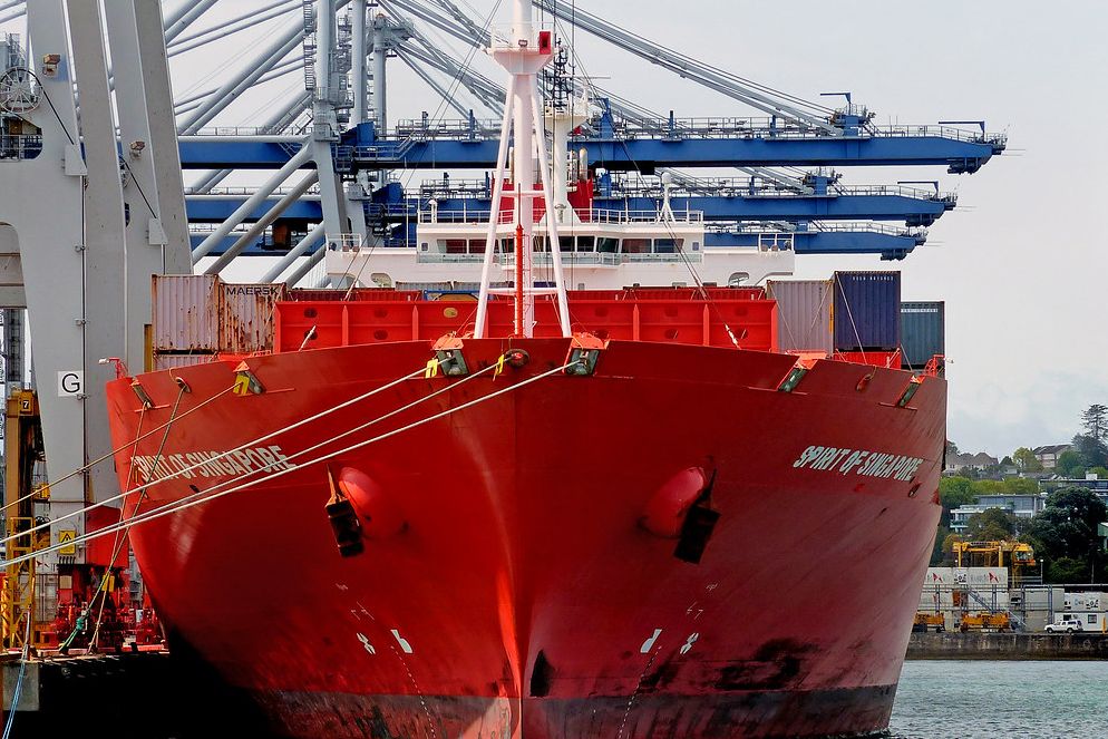 Red bow of a container ship under gantry cranes at the Port of Auckland